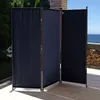 A three-panel black fabric room divider is set up on an outdoor patio with a view of the ocean in the background. Produktbild-Vorschau