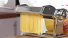 A close-up shot of a chrome pasta maker with spaghetti strands emerging from it. Produktbild-Vorschau