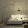 A modern living room scene featuring a white sectional sofa and a gold arc floor lamp. Náhled obrázku produktu