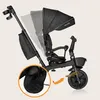 A black Lionelo Kori tricycle with a parent push bar and canopy, shown against a plain beige background. The image highlights adjustable features with ghosted overlays. Produktbild-Vorschau