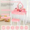 A pink and white children's vanity table and stool set with a mirror, displayed in a room with curtains and a basket of pillows. Voir les images du produit