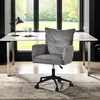 A grey corduroy office chair is placed in front of a white desk with a lamp and an open book on it. A large window with a view of greenery is behind the desk. Náhľad obrázku produktu