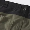 A close-up view of the waistband and pocket of a pair of olive green shorts. Produktbild-Vorschau