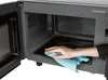 A hand is cleaning the inside of a microwave oven with a blue cloth. Produktbild-Vorschau