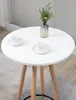 A white round table with wooden legs, set with two cups and saucers and a vase of flowers. Podgląd zdjęcia produktu