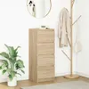 A tall, narrow wooden dresser with four drawers stands against a white wall. A large green plant is to the left, and a coat rack with a coat and bag is to the right. A round mirror hangs on the wall above the dresser. Podgląd zdjęcia produktu