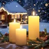 Three LED candles on a wooden surface with pine branches and fairy lights, in front of a snowy cabin with Christmas lights. Voir les images du produit