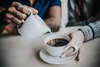 A person is pouring cream into a cup of coffee. Podgląd zdjęcia produktu