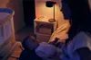 A mother holding her baby next to a crib, with a nightstand featuring a lamp and a sound machine. Náhľad obrázku produktu