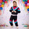 A man wearing a retro tracksuit poses in front of a white background decorated with balloons, streamers, and confetti. Anteprima dell’immagine prodotto