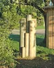 Wooden posts are arranged in a cluster in a garden setting, with greenery and a wooden structure in the background. Produktbild-Vorschau
