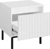 A white nightstand with a fluted drawer front and black legs, shown from a three-quarter angle with the drawer slightly open. Náhled obrázku produktu