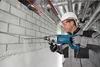 A construction worker is using a Bosch hammer drill to drill into a brick wall in an industrial setting with pipes overhead. Voir les images du produit