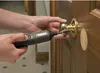 A person is using a cordless electric screwdriver to install a doorknob on a wooden door. Produktbild-Vorschau