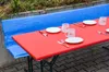 A table set for a meal outdoors, with plates, cutlery, and cups arranged on a red tablecloth. Produktbild-Vorschau