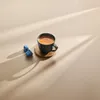 A cup of espresso coffee and two coffee capsules on a light beige surface with dramatic shadows cast by light beams. Produktbild-Vorschau