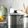 A stainless steel pot with a glass lid and black handle sits on a black stovetop. Podgląd zdjęcia produktu
