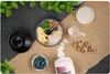 A flat lay of ingredients for a smoothie or oatmeal bowl, including a blender base, oats, bananas, blueberries, walnuts, spinach, and a container of protein powder. Náhľad obrázku produktu