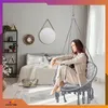 A woman sits in a hanging chair in a bedroom setting. Voir les images du produit