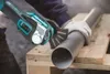 A person wearing gloves is using a Makita multitool to cut a pipe that is resting on wooden planks. Produktbild-Vorschau
