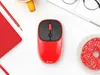 A red computer mouse is placed on a white surface, surrounded by other office and food items. Produktbild-Vorschau