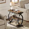 A narrow, three-tiered side table with a wood top and black metal frame, placed next to a sofa in a living room setting. It is decorated with a lamp, a cup of coffee, cookies, and a basket of flowers. Anteprima dell’immagine prodotto