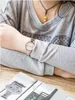 A person wearing a watch is sitting at a table with a magazine. Produktbild-Vorschau