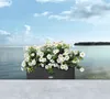 A planter box filled with white flowers sits on a ledge overlooking a body of water. Produktbild-Vorschau