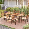 An outdoor dining set with a wooden table and chairs, set on a patio with flowers in the background. Náhled obrázku produktu