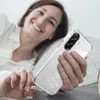 A woman is lying in bed, smiling and holding a transparent phone case with a Samsung phone inside. Produktbild-Vorschau