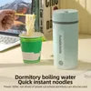 A person is holding chopsticks with noodles over a cup of instant noodles, with a portable kettle and books in the background. Produktbild-Vorschau