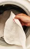 A hand holding a white cleaning cloth with a red Vileda logo, about to place it into a washing machine. Produktbild-Vorschau