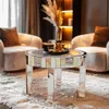 A mirrored round coffee table with a gold tray and glasses on top, placed on a fluffy rug in a living room setting with chairs and decorative plants in the background. Anteprima dell’immagine prodotto