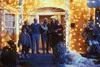 A group of people standing on the steps of a house decorated with Christmas lights. Podgląd zdjęcia produktu