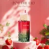 A perfume bottle with a straw and lid resembling a drink, surrounded by strawberries and foliage, on a pink background. Voir les images du produit