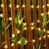 A string of flower-shaped solar lights attached to a wooden fence, with green foliage. Produktbild-Vorschau