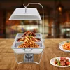 A chafing dish with three compartments filled with food, set on a wooden table with plates of food in the foreground and background. Podgląd zdjęcia produktu