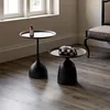 Two black side tables are placed on a wooden floor next to a window and a chair. Podgląd zdjęcia produktu
