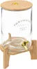 A clear glass beverage dispenser with a bamboo lid and stand, featuring a gold spigot. Produktbild-Vorschau