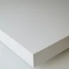 A close-up, angled view of a white furniture piece, likely a TV stand or cabinet, against a light gray background. Produktbild-Vorschau