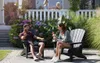 A couple relaxing on a patio in Adirondack chairs, with children visible in the background on a porch. Produktbild-Vorschau