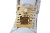 Close-up of the front of a white and gold Nike Air Jordan 1 Retro High sneaker, focusing on the laces and a decorative gold charm. Podgląd zdjęcia produktu