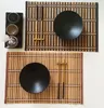 A top-down view of two bamboo placemats with black bowls and chopsticks. Produktbild-Vorschau