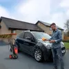 A man is washing a car in front of a house. Produktbild-Vorschau