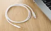 A white AUX cable with a Lightning connector and a 3.5mm jack is coiled on a wooden surface next to a laptop. Produktbild-Vorschau