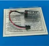 A battery with wires attached, packaged in clear plastic on top of a white and gray paper insert with text. Náhled obrázku produktu