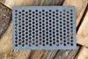 A gray metal grate with many small holes is placed on top of stacked pieces of wood. Náhled obrázku produktu