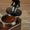 A hand is holding a coffee tamper over a portafilter filled with coffee grounds. Náhled obrázku produktu