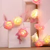 A string of rose-shaped LED lights draped over a white gift bag with a flamingo silhouette, adorned with pink feathers. Produktbild-Vorschau