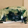 Toy figures of dragons and a lion are arranged inside a makeshift tent made from a light green sheet with dark green cat-like silhouettes. Voir les images du produit